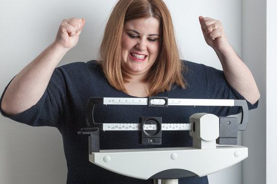 Woman celebrating weight loss raising arms on the scale