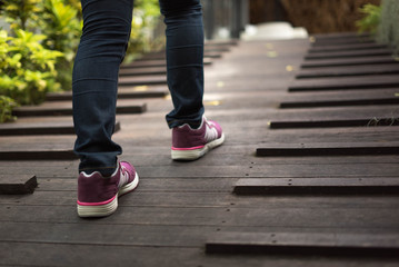 women wearing jeans and sneakers step on old wooden bridge