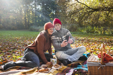 Happy mature couple taking selfie through mobile phone in forest during picnic