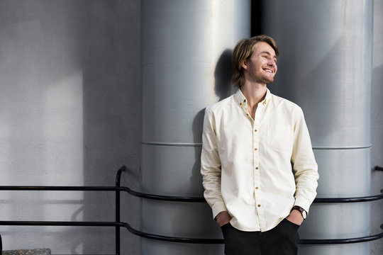 Smiling young male student with hands in pockets leaning against columns