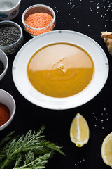 Cream soup of assorted lentil. Yellow and green lens, spices as raw for meal and lemon on black background. Healthy, appetizing, delicious, vegetarian food. Top view, copy space.
