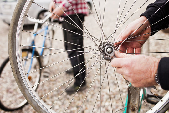 Cropped image of senior man repairing bicycle tire with son working in background
