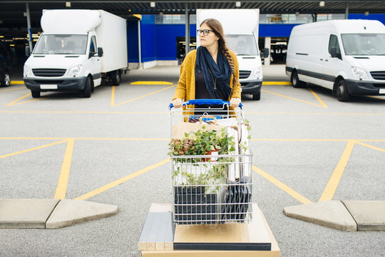 Young woman pushing trolley full of purchases in car park