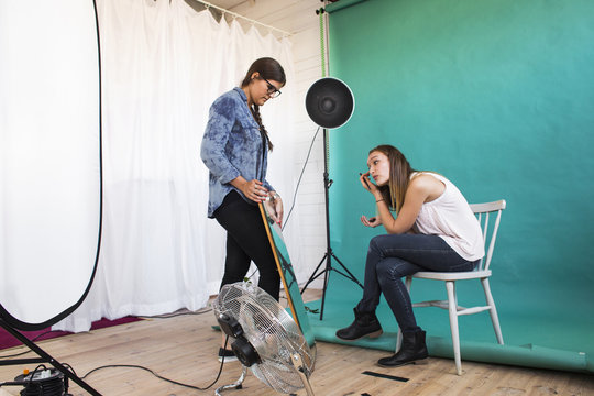 Photo assistant holding mirror for fashion model applying make-up in studio