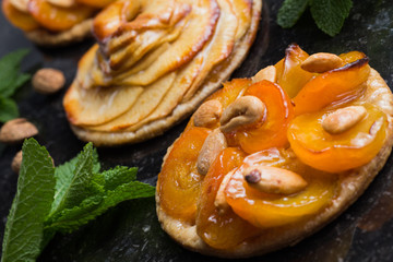 Tart with apricot and apple. Traditional french pie with fruits on dark marble background. Decorated almonds and mint leafs. Delicious dessert with copy space closeup.
