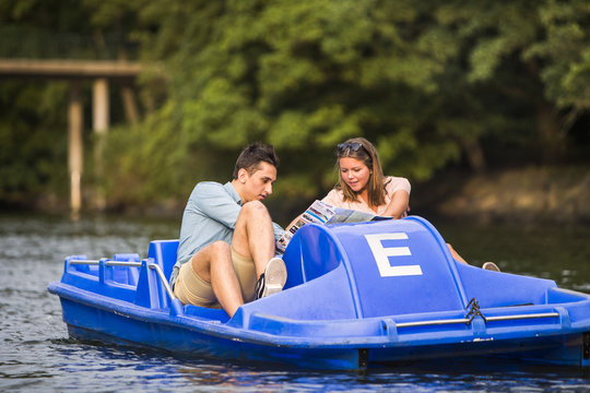 Friends pedal boating on river against trees