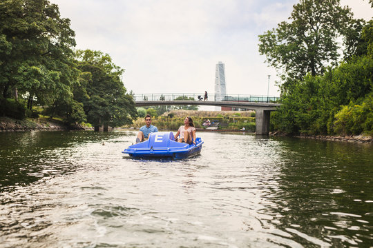 Couple pedal boating on river against bridge in city