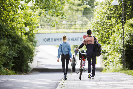Rear view of couple with bicycle walking on street