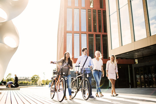 Young friends with bicycles walking outside concert hall in Malmo Live