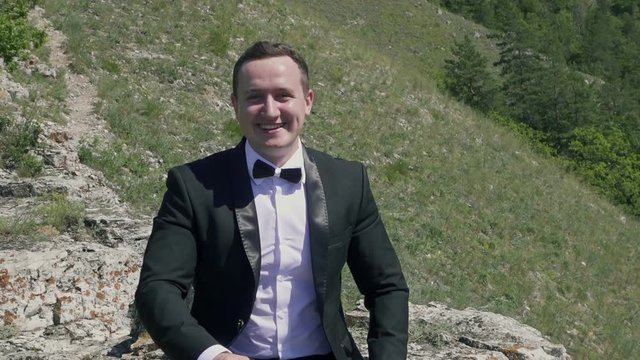 Slow motion video of  smiling happy groom with his thumbs up on the background of beautifull Mountain View. Full Hd stock footage clip.
