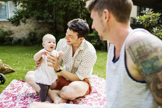 Two men with baby girl having picnic outdoors