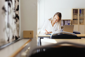 Young woman writing at desk in classroom