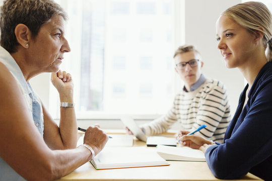 Side View Of Mature Teacher Looking At Student In Classroom