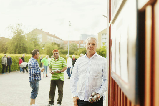 Portrait of mature man holding balls while playing boule with friends at park