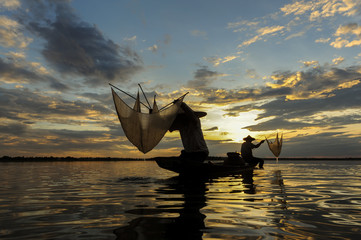 A fisherman casting a nets into the water during sunrise