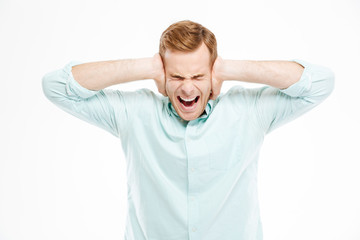 Irritated stressed young man covered ears by hands and shouting