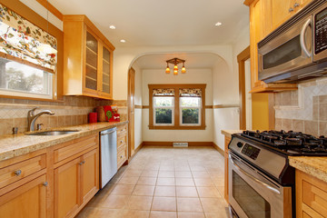Light brown tones kitchen interior with tile floor and steel appliances.