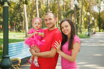 Family is walking in park. Father and mother holding daughter outdoors in summer. Parent love and care. Happy kid, childhood. Photo with copy space.