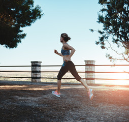 Young energetic female in sportswear jogging at sunset in the park. Concept of dieting, health and fitness. 