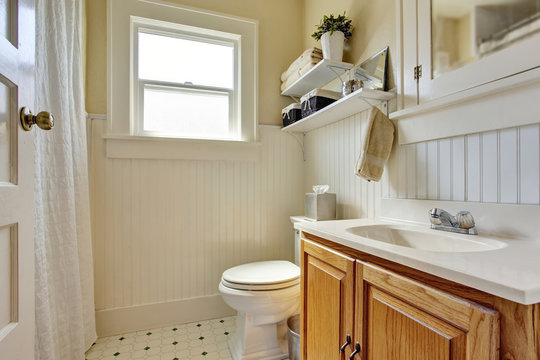 Bathroom design in creamy colors with brown wooden cabinet and small window.