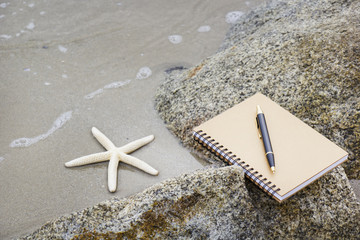 Notebook, pen and starfish on the beach in vacation