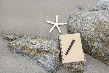 Notebook, pen and starfish on the beach in vacation