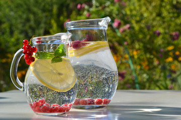 Infused fruit water. Refreshing summer homemade cocktails in glass jugs on outdoor background.