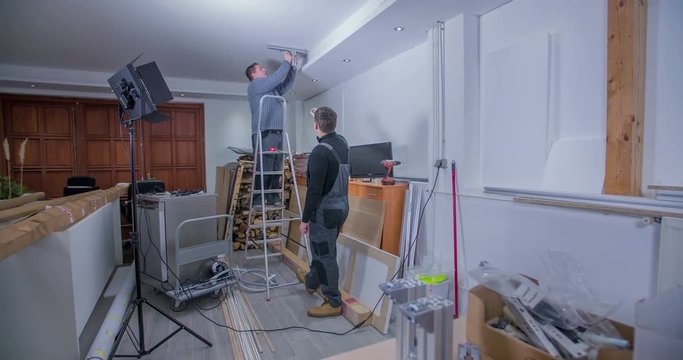 Two men are building a home studio for different photo and video shootings. There are many tools around. Wide-angle shoot.
