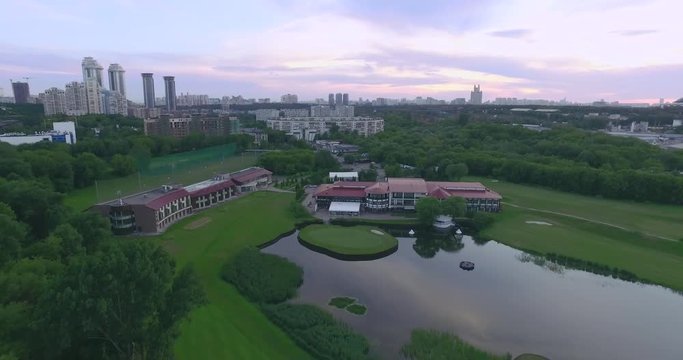Aerial view of golf course with pond situated in the city during beautiful sunset. Reflection of the sky and clouds in pond surface. Moscow, Russia.