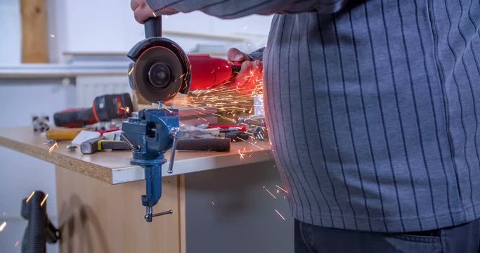 A man is polishing an object with a machine. Sparks are falling everywhere around. Close-up shot.
