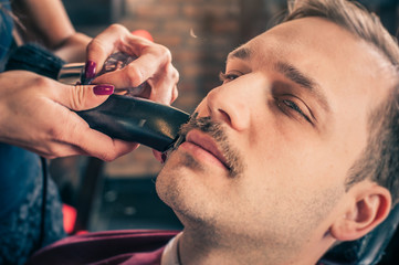 Female barber cut a client's mustache with trimmer in a barber shop. Close-up