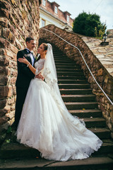 Romantic valentyne couple, bride and groom posing at old stairs and stone wall. Newlyweds  embracing and kissing.