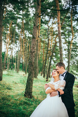 Young wedding couple enjoying romantic moments outside on a summer meadow. Copy space. Pine forest. Green forest are kissing photo portrait. Bride and groom