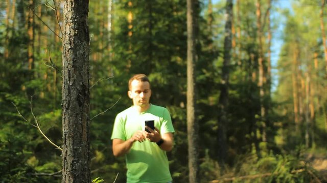 A man walks through the forest with the phone and looks at the navigation application. He chooses the right direction