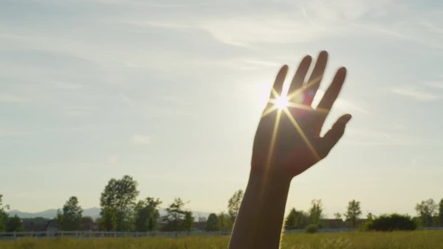SLOW MOTION: Sun shining through fingers of a waving hand