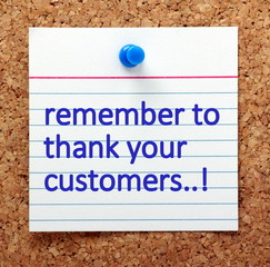 The words Remember to Thank Your Customers in blue text on a note card pinned to a cork notice board as a reminder