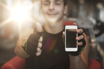 young man with smartphone showing thumbs up in gym