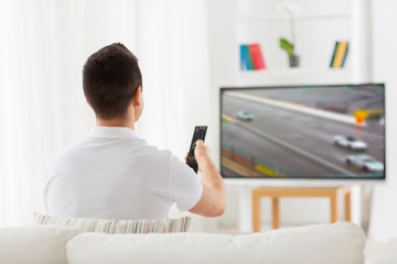 man with remote watching motorsports on tv at home