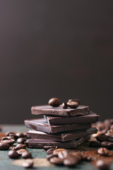 Stack of chocolate chunks with coffee beans on a wooden background, closeup