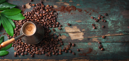 Hot coffee in a coffeepot or turk on a wooden background with coffee leaves and beans, horizontal...