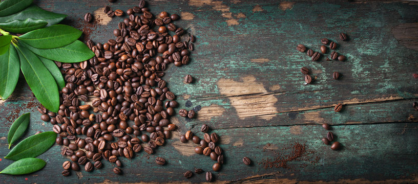Roasted coffee beans with green leaves on a vintage background, top view with copy space