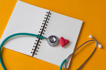 Red heart , notebook and a stethoscope on yellow background