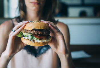 Young girl holding in female hands fast food burger, american unhealthy calories meal on blue background, mockup with space for text message or design, hungry human with grilled hamburger front view