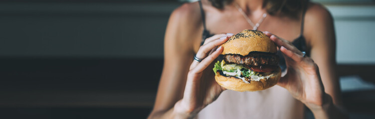 Young girl holding in female hands fast food burger, american unhealthy calories meal on blue...