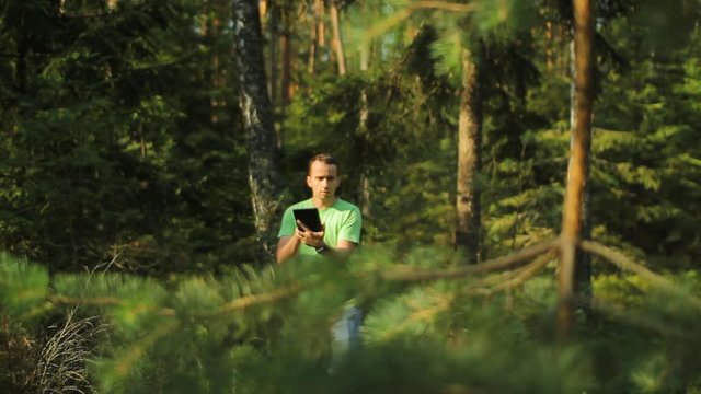 A man walks through the forest with a tablet PC and looking at the navigation application. He chooses the right direction