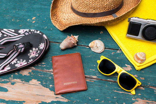 Strohhut, Flipflops, Reisepass, Fotoapperat und Muscheln auf Holzuntergrund
