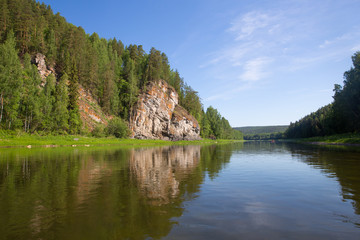 Fototapeta na wymiar blue sky, rock and forest reflected in calm surface of river