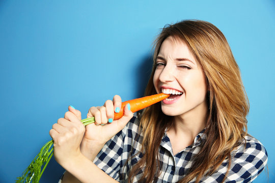 Beautiful girl eating carrot on blue background