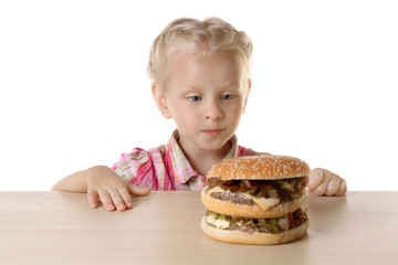 Funny little girl hiding behind  table and looking on big burger