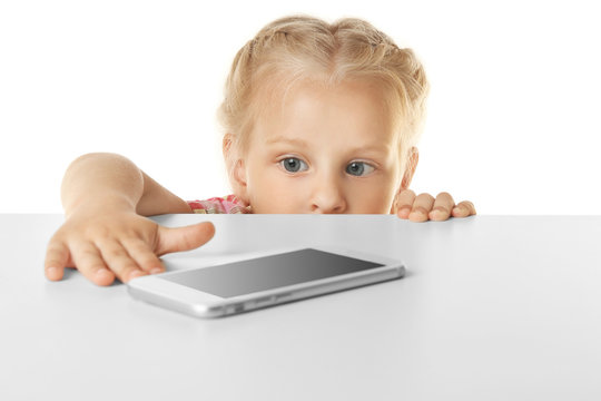 Funny Little Girl Hiding Behind White Table And Looking At Mobile Phone